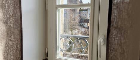 A window with a view of a building with a tower, a balcony, and a door.