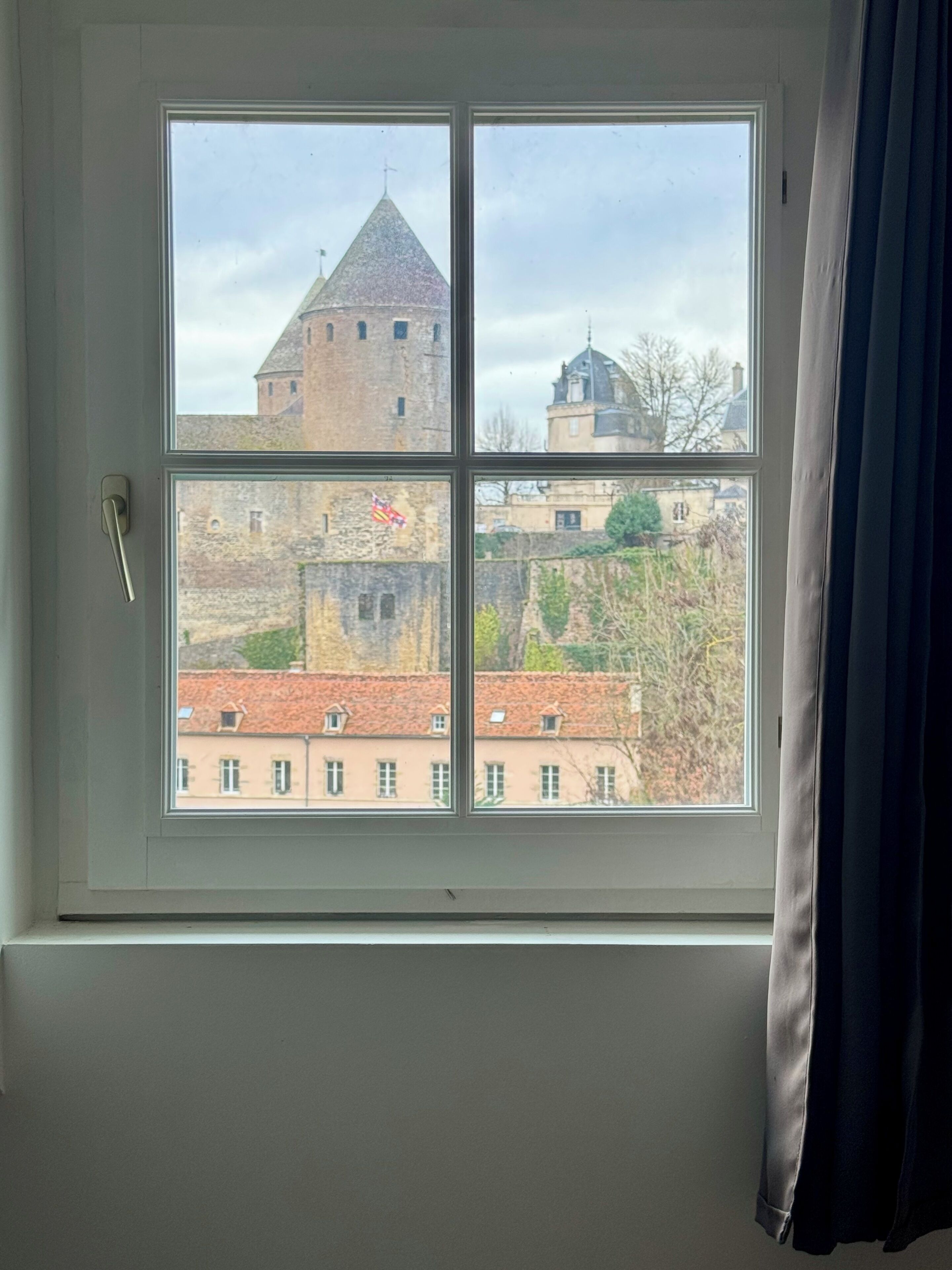 Una ventana con vistas a un edificio histórico con una torre y una bandera.