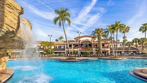 A resort pool with a water feature, palm trees, and a building with a red-tiled roof. - Beautiful 2 BR condo in Orlando minutes from all attractions. (Orlando)