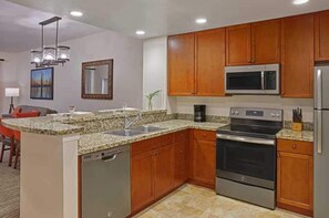 Eine moderne Küche mit Granit-Arbeitsplatten, Edelstahlgeräten, Holzschränken und einem eingebauten Geschirrspüler.