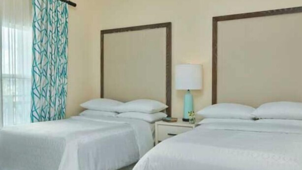 A hotel room with two beds, a nightstand with a lamp, and a window with curtains. - Beautiful 2 BR condo in Orlando minutes from all attractions. (Orlando)