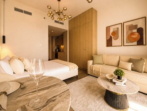 A modern living room with a sofa, a dining table with a glass top, and a kitchen in the background. - Modern Chic Studio Apartment - JVC Dubai (Dubai)