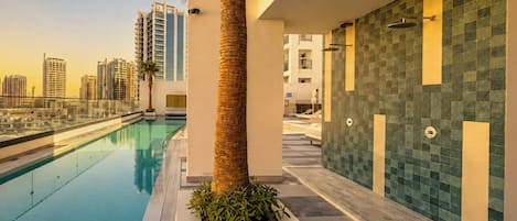 A modern pool area with a clear view of the city skyline, a palm tree, and a tiled wall.
