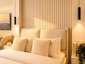 A modern bedroom with a large bed, a television mounted on the wall, and a bedside table with a lamp. - Modern Chic Studio Apartment - JVC Dubai (Dubai)