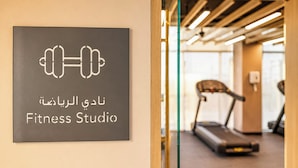 A sign for a Fitness Studio with a dumbbell icon and text in Arabic and English. - Modern Chic Studio Apartment - JVC Dubai (Dubai)