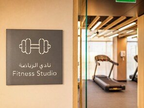 A sign for a Fitness Studio with a dumbbell icon and text in Arabic and English. - Modern Chic Studio Apartment - JVC Dubai (Dubai)