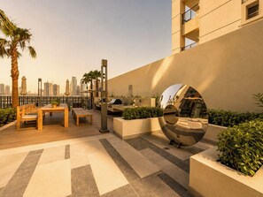 An outdoor patio with a wooden table and chairs, a grill, and a decorative mirror. - Modern Chic Studio Apartment - JVC Dubai (Dubai)