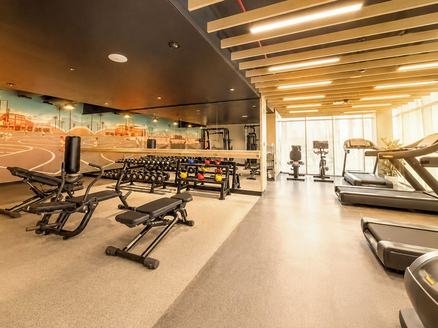 A gym with exercise equipment, treadmills, and a mural on the wall.