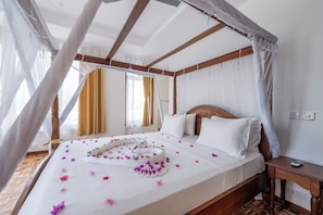 A four-poster canopy bed with white linens and floral decorations, a wooden headboard, and a nightstand with a phone. - Villa Branca Diani: Spacious 5-bedroom luxury with personalized service. (Diani Beach)