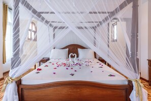 Ein Bett mit Baldachin, ein hölzernes Kopfteil, weiße Bettwäsche und eine zu einem Schwan geformte Handtuchanordnung.