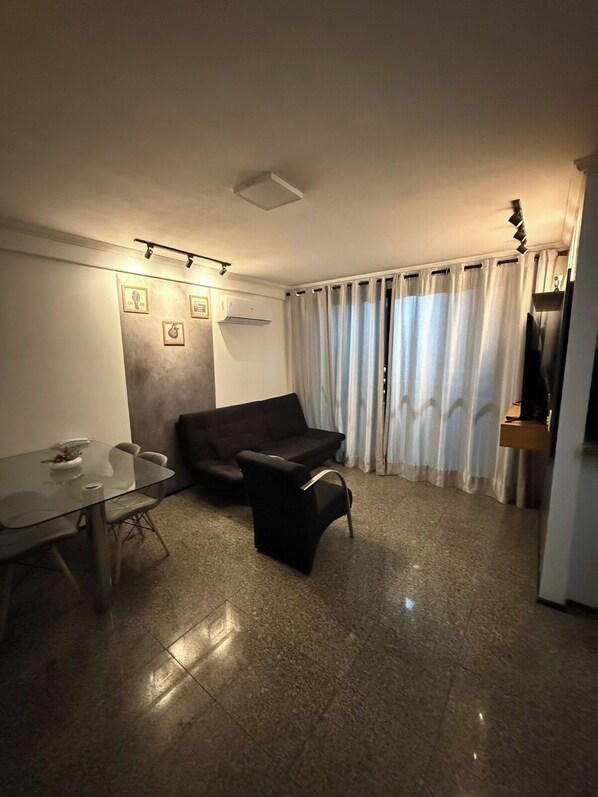 A modern living room with a glass dining table, a black sofa, and a large window with curtains. - 2-bedroom apartment in perfect Fortaleza with refreshing AC (Fortaleza)