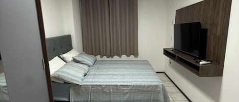Ein Schlafzimmer mit Bett, Vorhängen, Fernseher und Kleiderschrank.