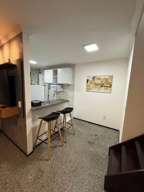 A compact kitchen with a microwave, white cabinets, and a bar stool area. - 2-bedroom apartment in perfect Fortaleza with refreshing AC (Fortaleza)