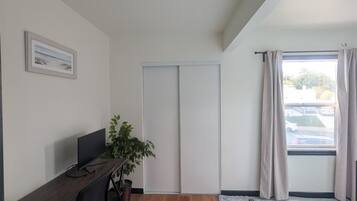 Une pièce comprenant un lit, un bureau avec un ordinateur, une plante en pot et une fenêtre avec des rideaux.