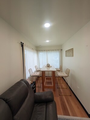 Un salon avec un canapé marron foncé, une table à manger en bois et six chaises, ainsi qu’un luminaire au plafond.