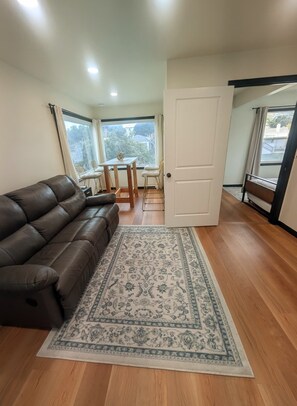 A living room with a brown leather sofa, a patterned rug, a dining table with chairs, and a view of the outdoors through a window. - Beautiful Cozy 2 Bedroom Home Retreat w/ H.T. Quick BART/SF/Berkeley Access (Richmond)
