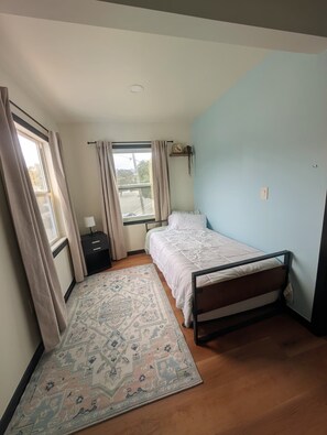 A bedroom with a bed, a nightstand, a window with curtains, and a patterned rug. - Beautiful Cozy 2 Bedroom Home Retreat w/ H.T. Quick BART/SF/Berkeley Access (Richmond)