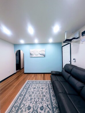 Ein Zimmer mit einer schwarzen Ledersofa, einem gemusterten Teppich, einem an der Wand montierten Projektor und einer Tür zu einem anderen Raum.