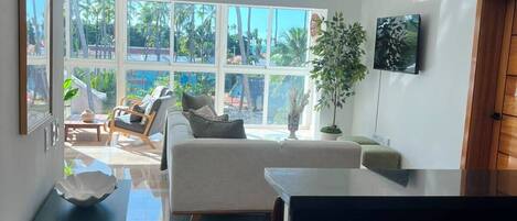 A modern kitchen with a large island, a dining area with a sofa and chairs, and a view of palm trees through large windows.