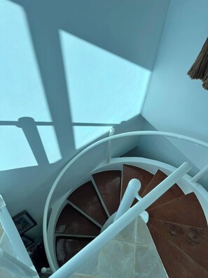 A spiral staircase with a white handrail and brown steps, leading upwards in a corner of a room with a sloped ceiling. - Beachfront Penthouse w/ Rooftop, Pools & Views (Punta Cana)