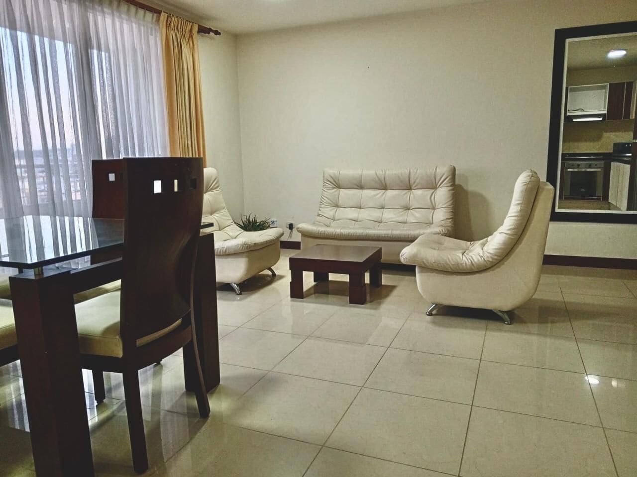 A living room with a sofa, two armchairs, a coffee table, and a dining table with chairs.