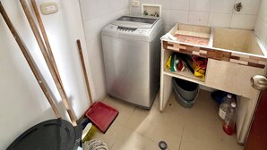 Pieni pyykinhuoltotila, jossa on pesukone, moppi, harja ja roskakori.