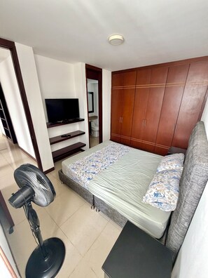 A bedroom with a bed, a TV, a wardrobe, and a standing fan. - Apto Lili - Cali - Wifi - Familiar, Piscina (Cali)