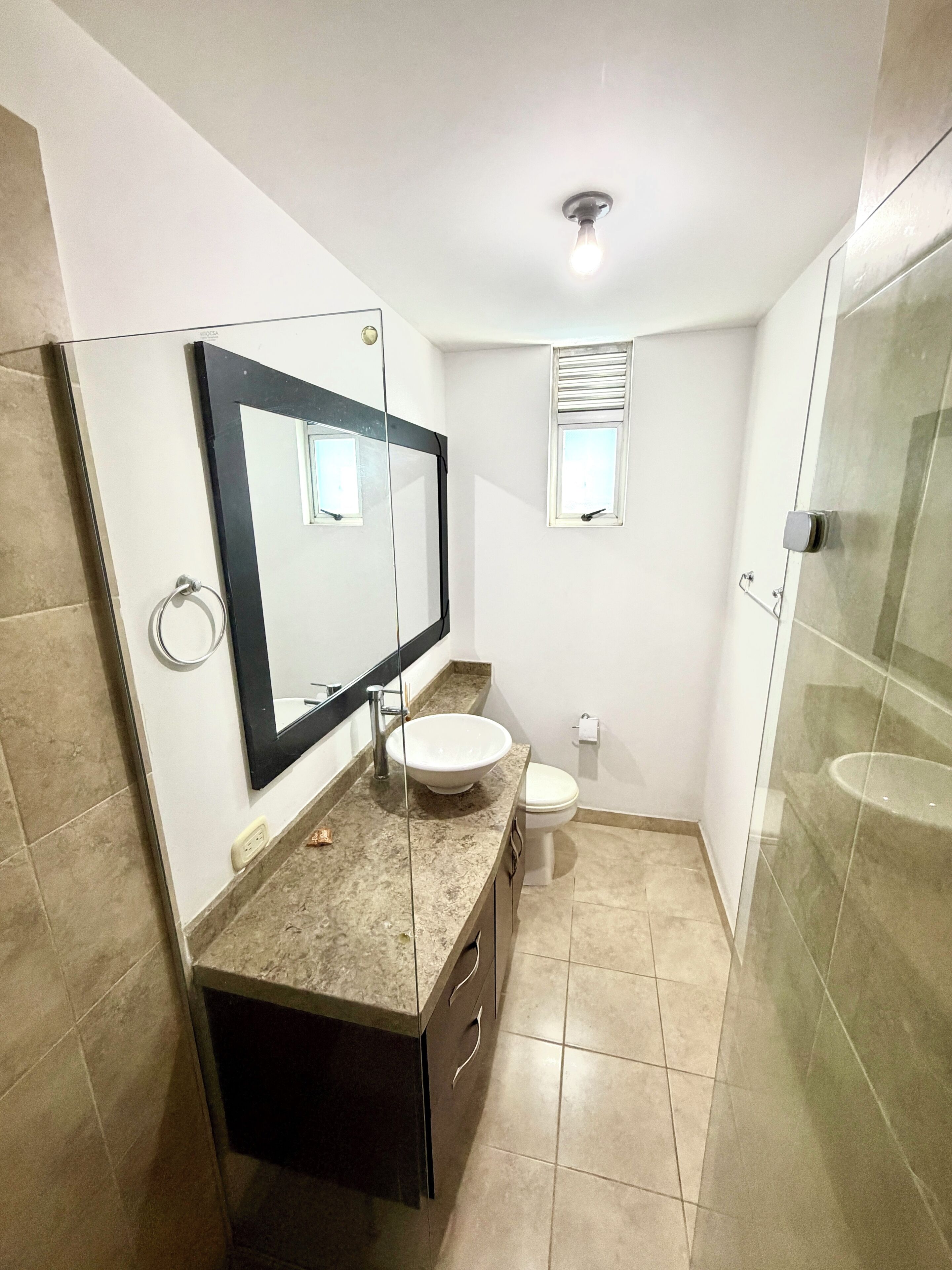 A bathroom with a large mirror, a sink, a toilet, and a shower area.