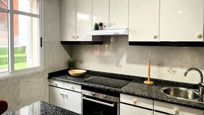 A modern kitchen with white cabinets, a granite countertop, a stainless steel sink, and a window with a view of a green landscape. - Quiet family house close to the historic centre, thermal baths and hospital (Ourense)
