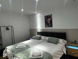 A modern hotel room with a large bed, bedside tables, a wall-mounted artwork, and a clothing rack.