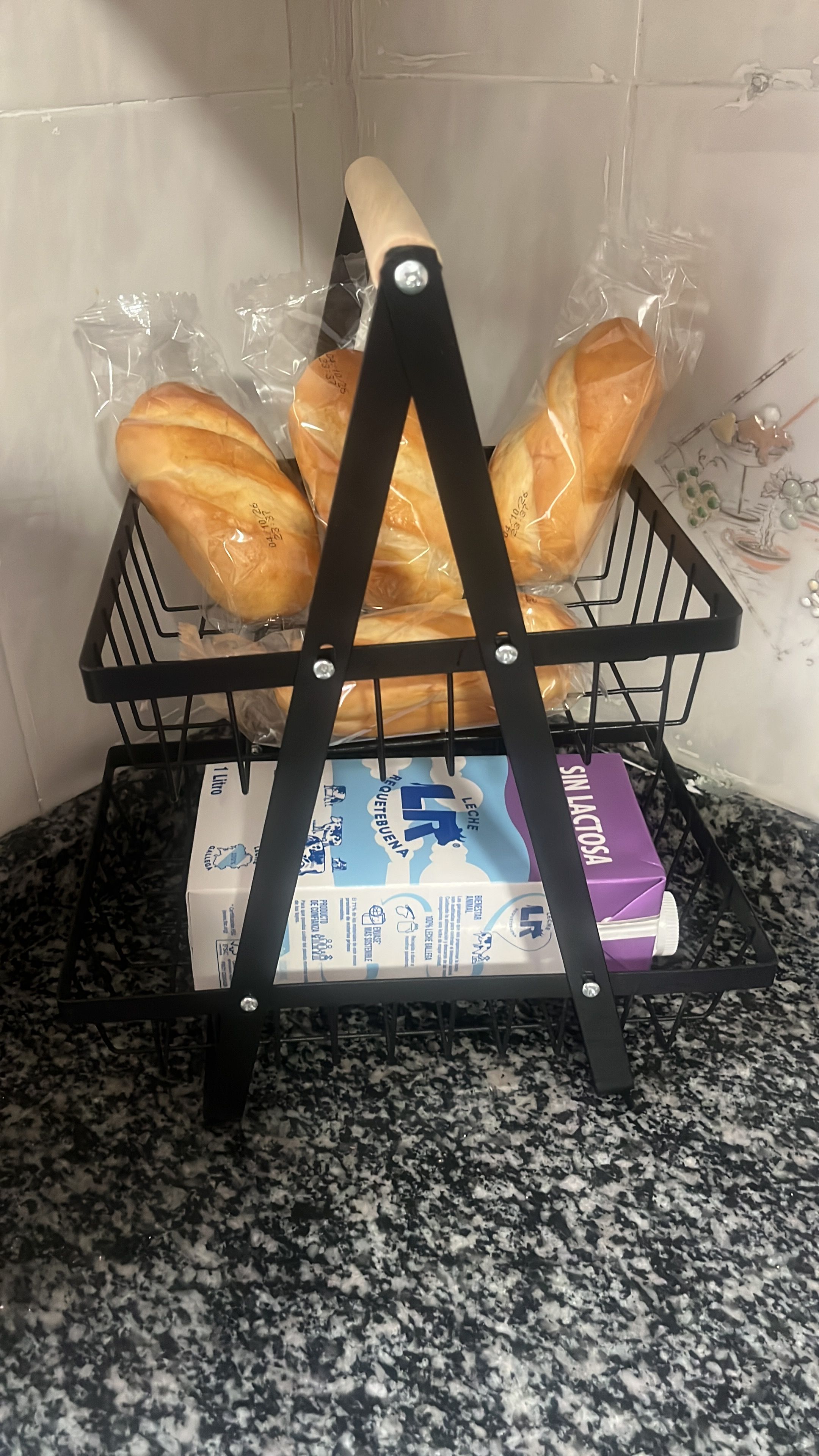 Un porta panes metálico negro con bolsas de plástico que contienen pan sobre una encimera de granito.