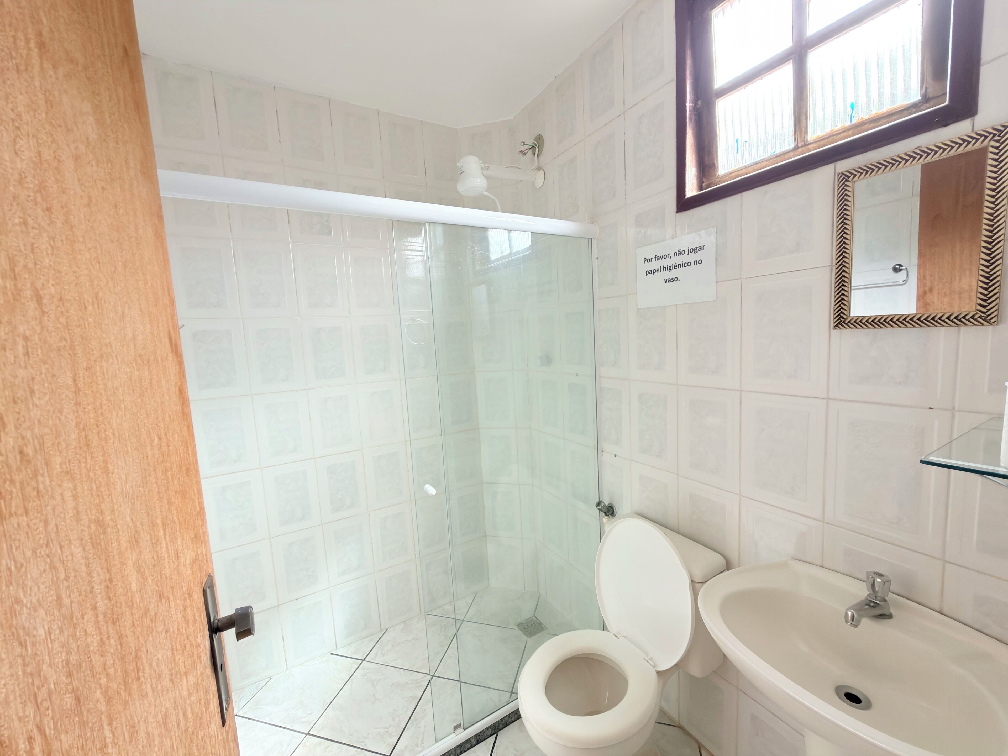 Een badkamer met een douchecabine van glas, een toilet, een wastafel en een spiegel met decoratieve lijst.