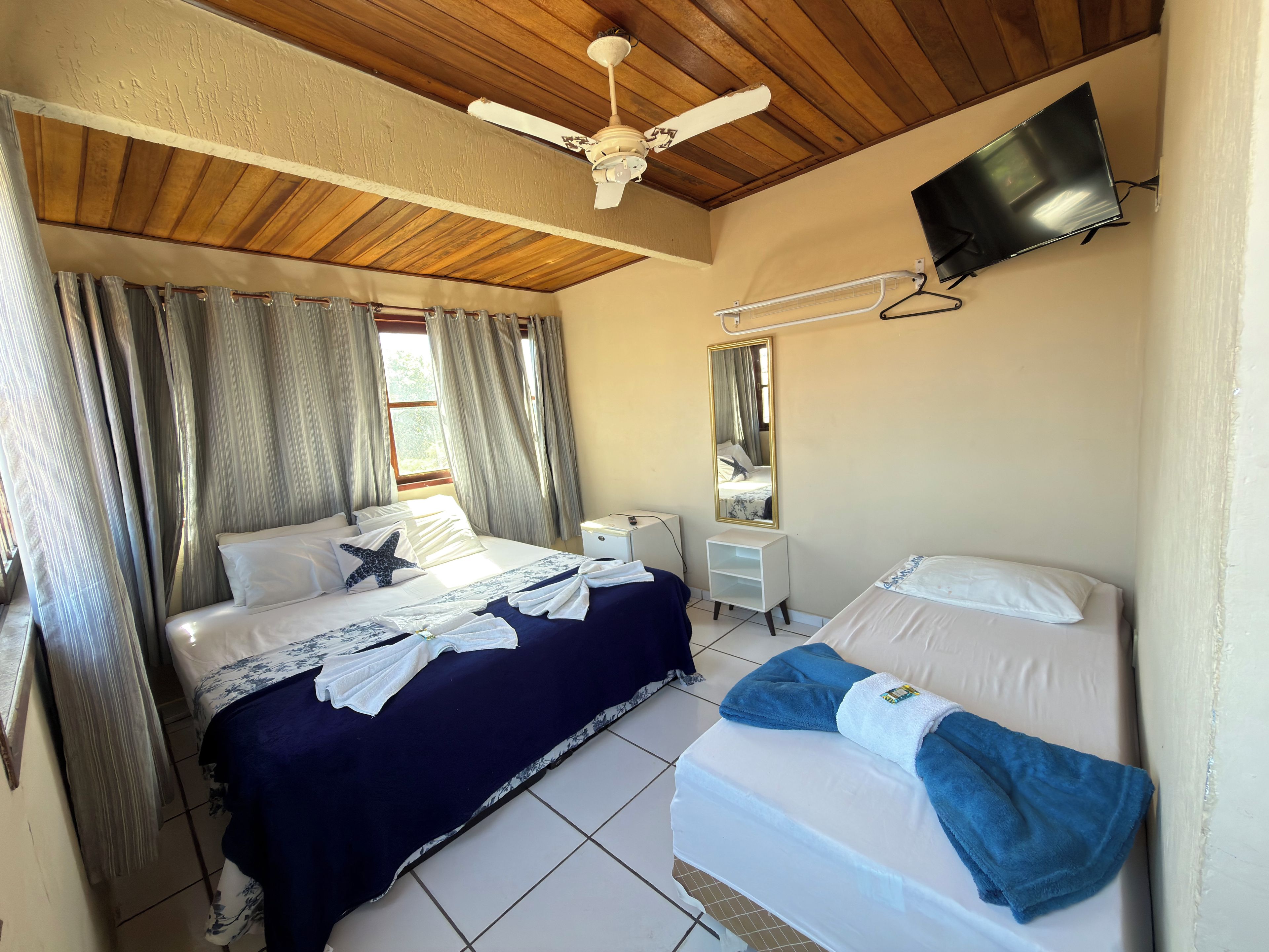 A hotel room with a bed, a smaller bed, a TV, a ceiling fan, and curtains.