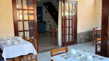 Un comedor con mesas preparadas para dos, sillas de madera y una pared de piedra.