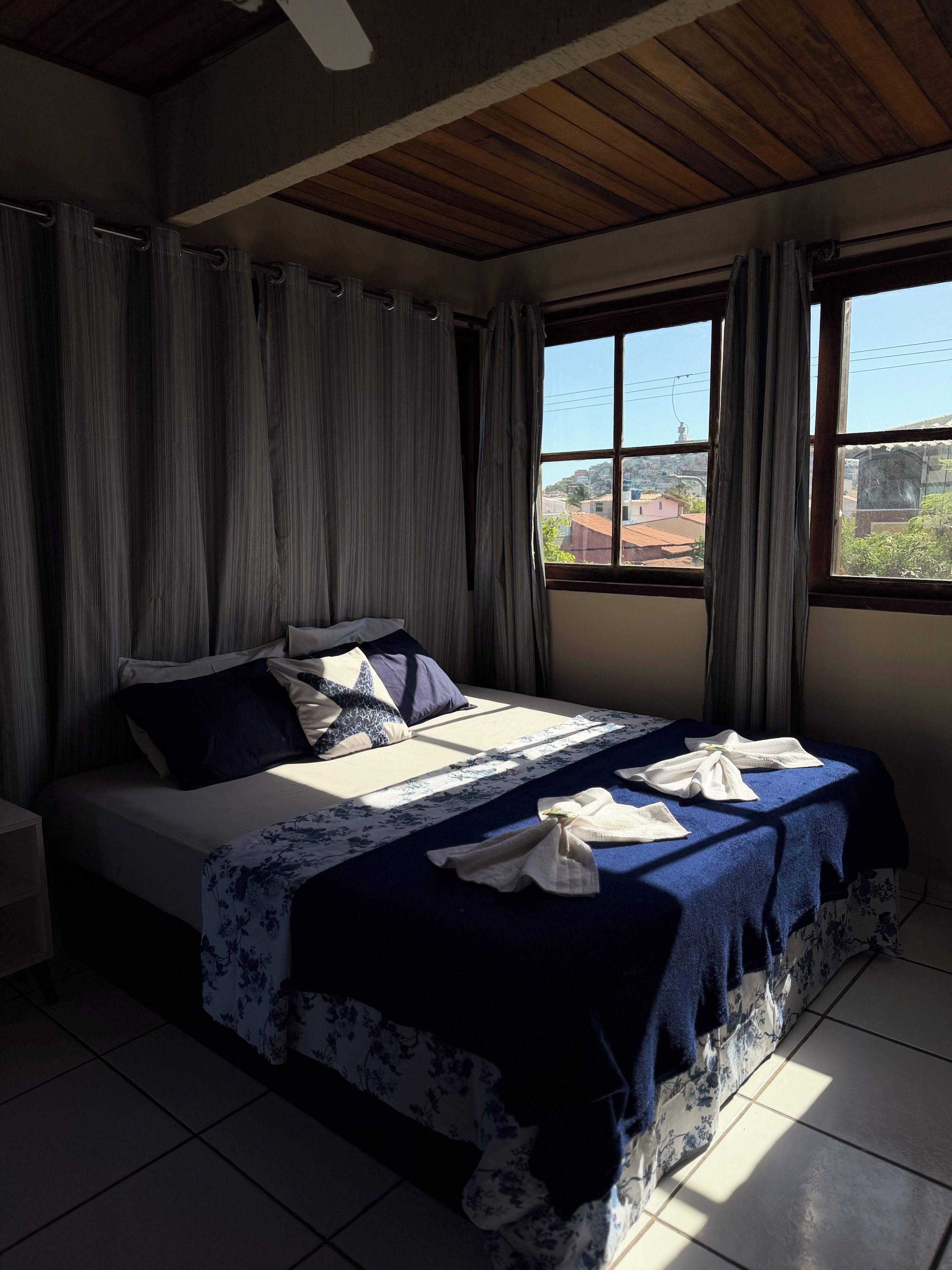 A bedroom with a bed, curtains, a window, and a view of the outside.