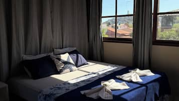 A bedroom with a bed, curtains, a window, and a view of the outside.