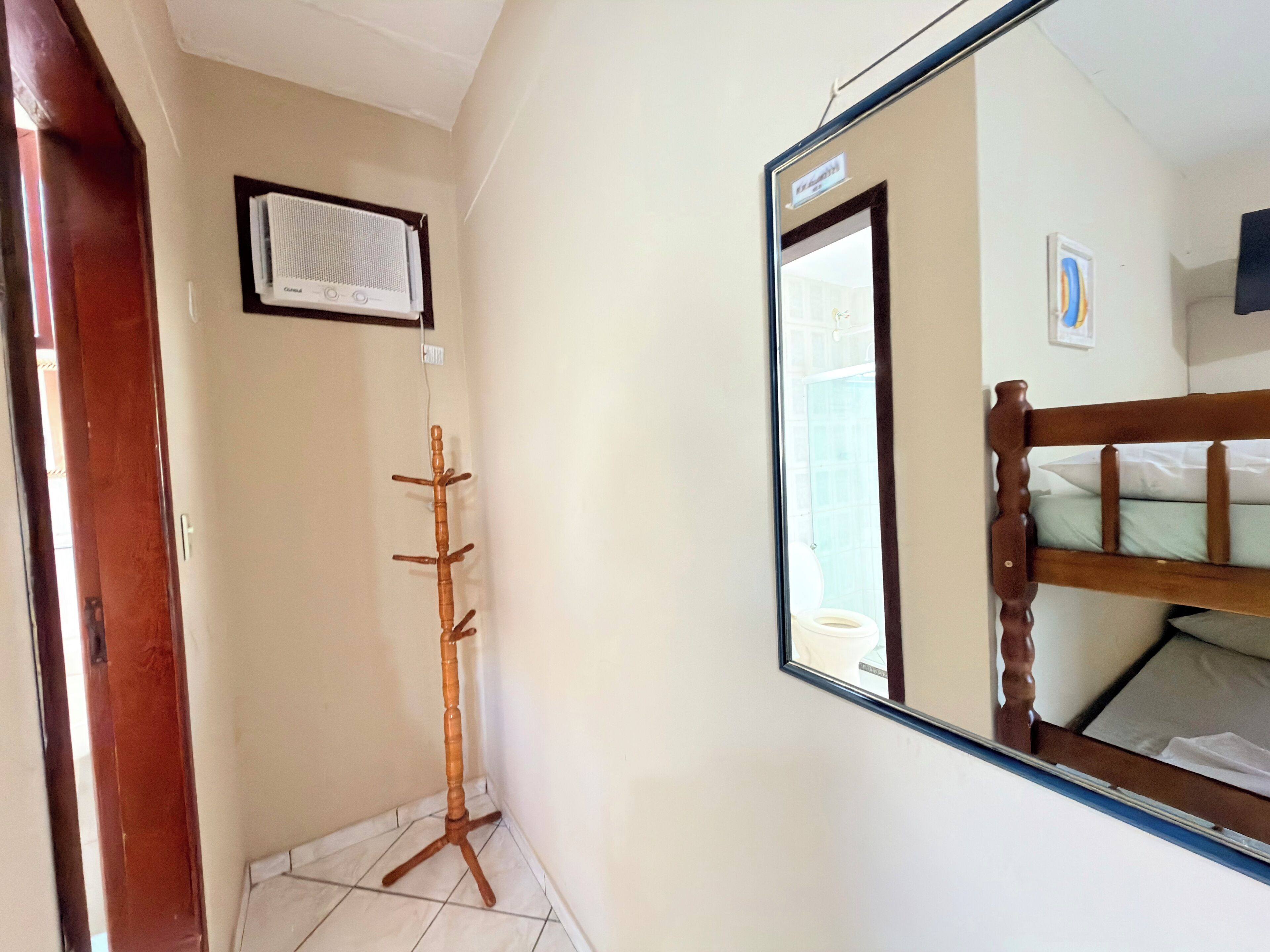 Una habitación con un perchero de madera, un espejo y una cama litera.