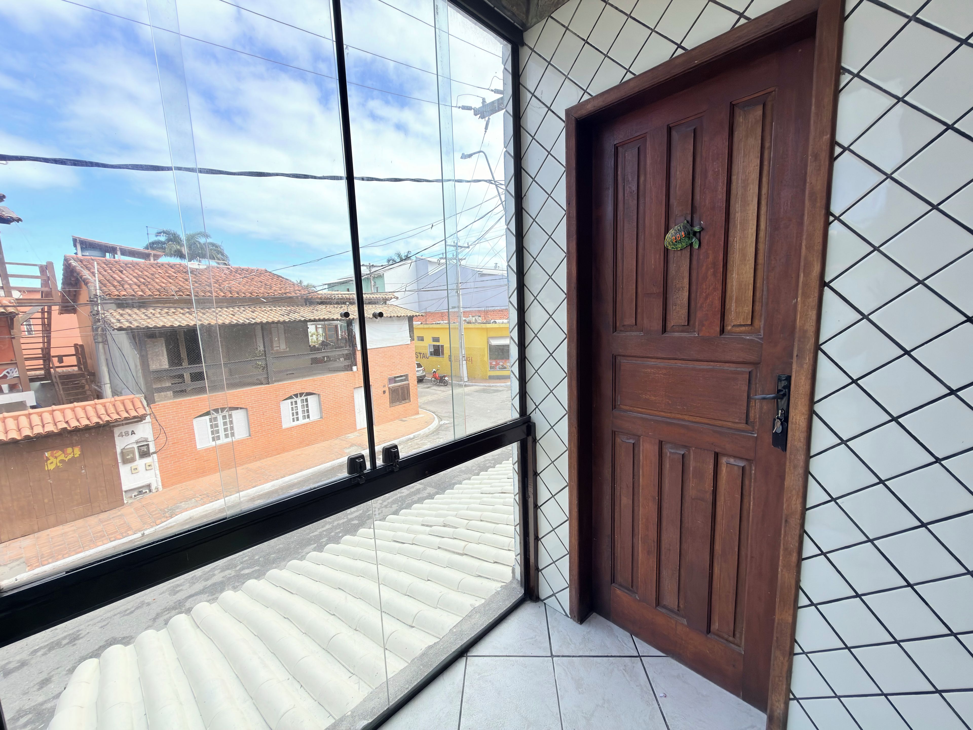 Une pièce avec une porte en bois, une fenêtre donnant sur des immeubles et un sol carrelé.