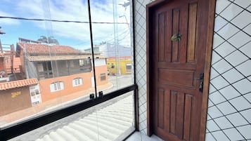 Une pièce avec une porte en bois, une fenêtre donnant sur des immeubles et un sol carrelé.