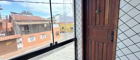 Um quarto com porta de madeira, janela com vista para edifícios e piso ladrilhado.