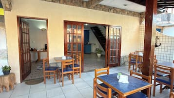 Un espace extérieur abrité, aménagé pour les repas, avec des tables et des chaises en bois, des murs en pierre et un sol carrelé.
