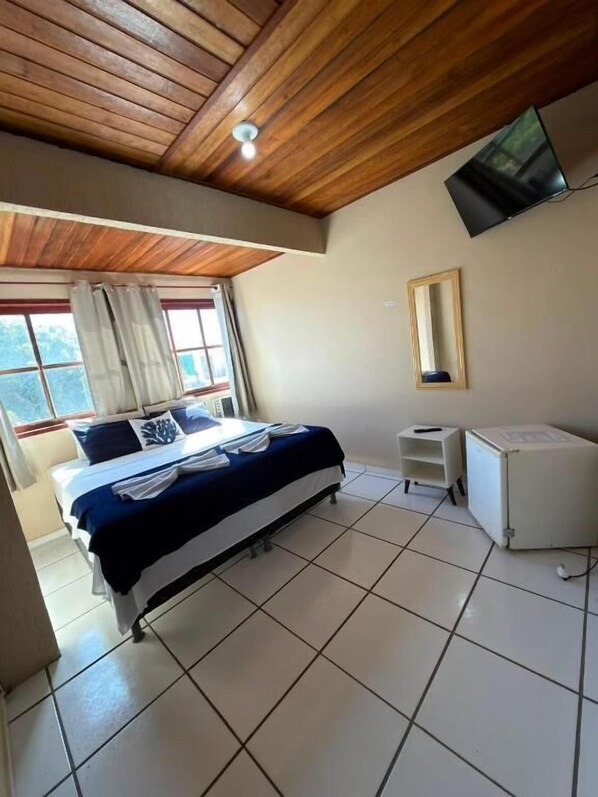 A hotel room with a bed, a desk, a television, and a window with curtains.