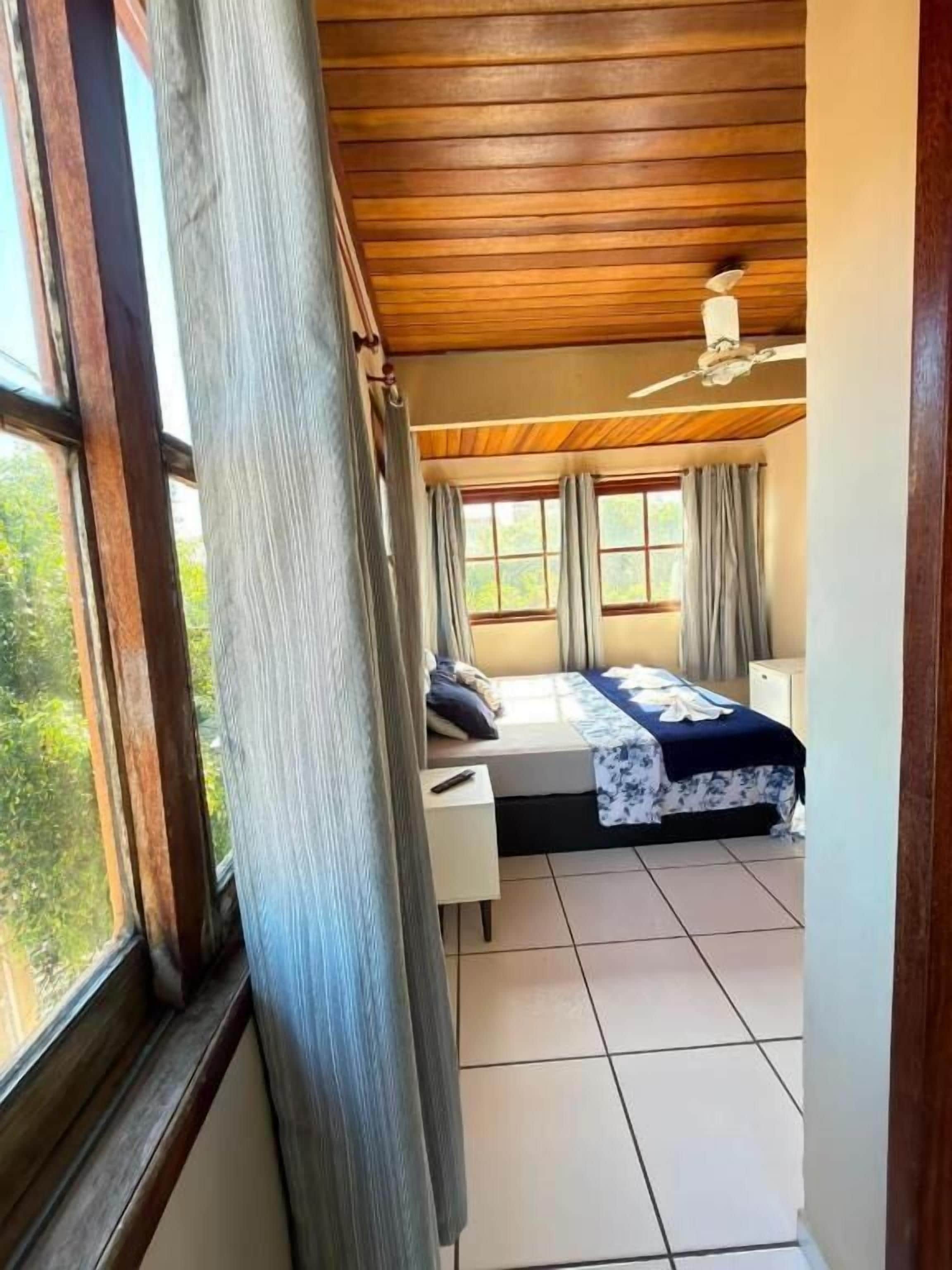 Een slaapkamer met een bed, nachtkastje, raam en plafondventilator.