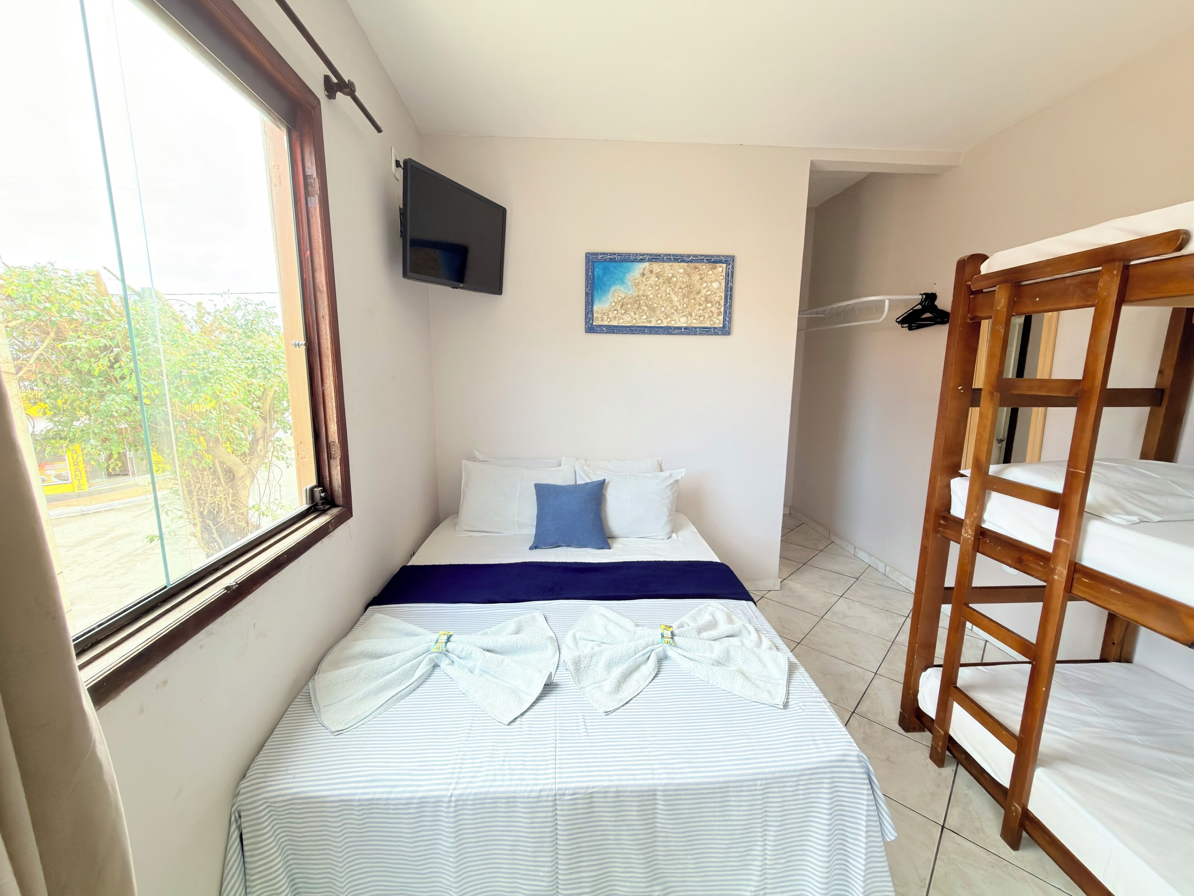Una habitación de hotel pequeña con cama, ventana, televisor empotrado y una cama litera de madera.