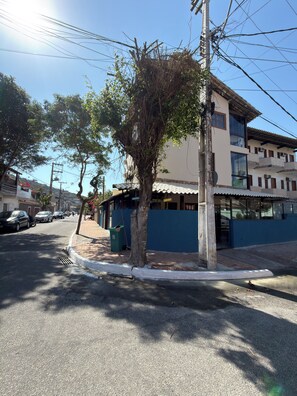 A street view with a building featuring a balcony, a tree, and parked cars.