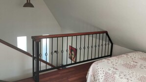 Ein Schlafzimmer mit einer Holztreppe, einem Bett mit floralem Überwurf, einer gelben Pendelleuchte und einer schwarzen Deckenleuchte.