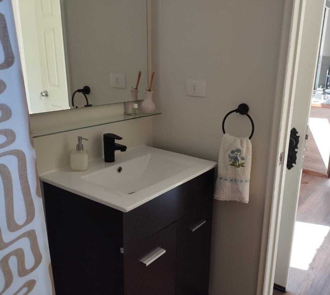 A bathroom with a white sink, dark cabinet, mirror, and a towel hanging on a hook.
