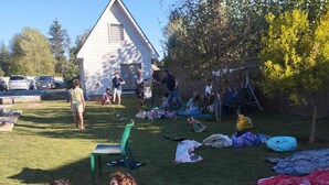 Un grup de persones reunides a l'aire lliure, algunes assegudes a l'herba, d'altres en cadires i unes quantes més estirades sobre mantells.