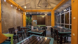A restaurant with wooden tables and chairs, a ceiling fan, and a view through large windows. - Ocean Reach Holidays (Mirissa)