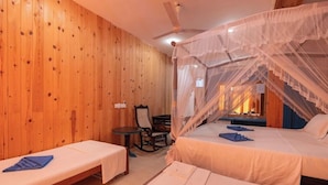 A room with wooden walls, a bed with a mosquito net, a chair, and a small table. - Ocean Reach Holidays (Mirissa)